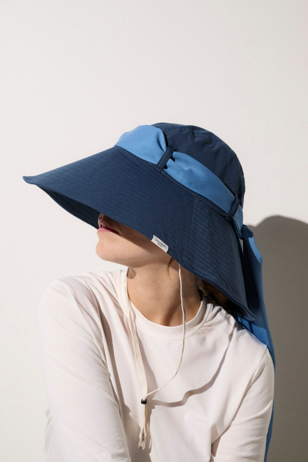 Femme portant un chapeau anti-UV bleu avec un ruban bleu clair. Idéal pour une protection efficace contre les rayons du soleil.