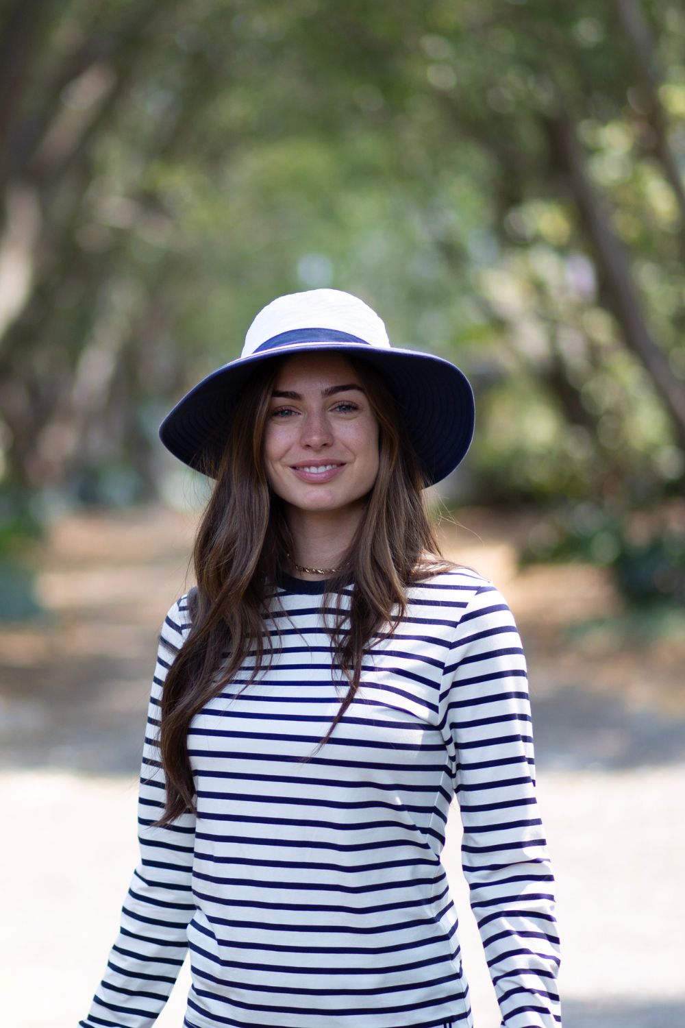 Femme souriante portant un t-shirt anti-UV rayé et un chapeau ensoleillé, idéale pour la protection solaire UPF 50+.