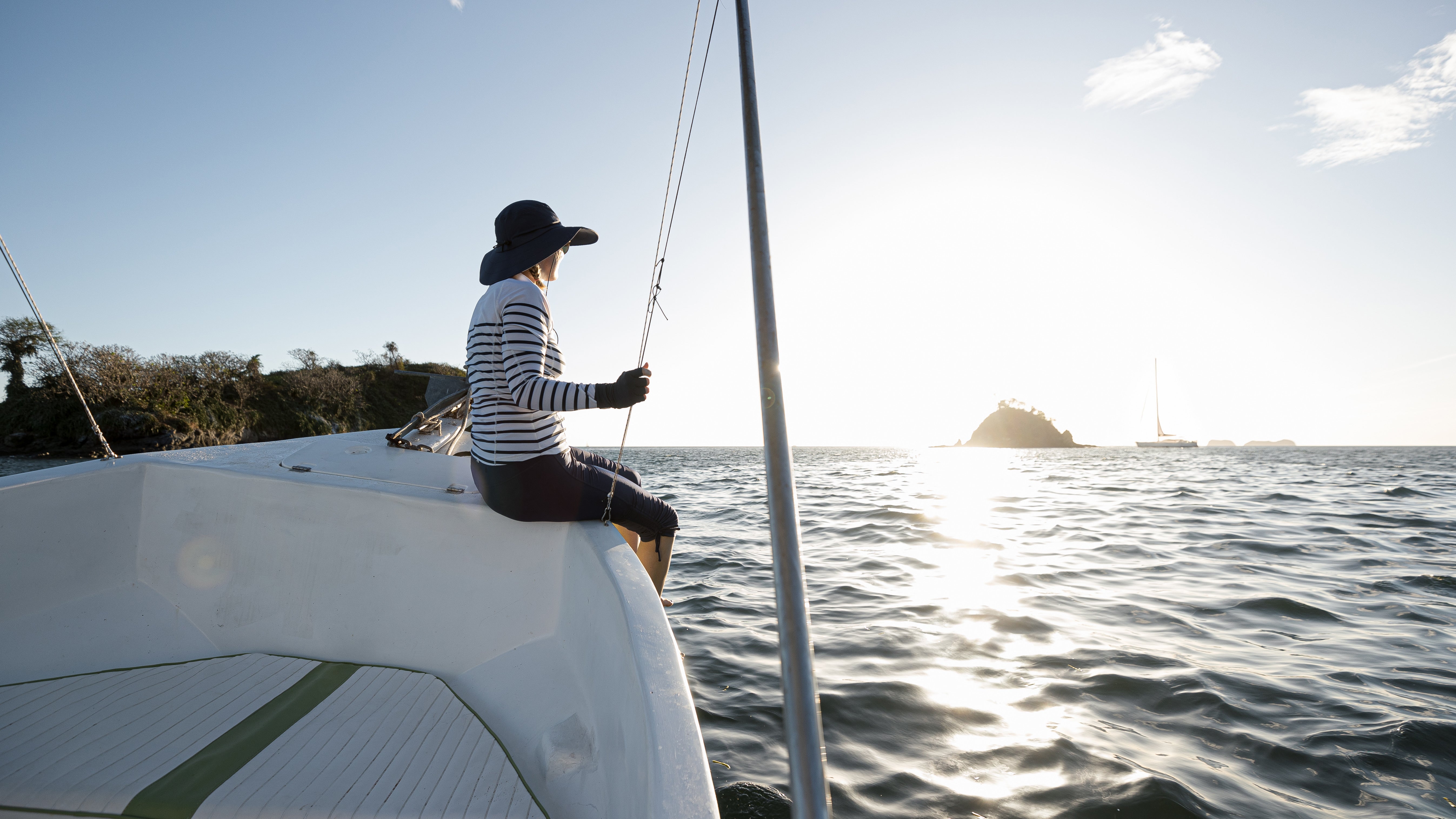 Femme sur un voilier, protégée par des vêtements et un chapeau anti-UV