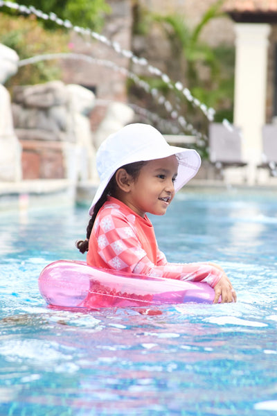 T-shirt de bain anti-UV - Fidji pour enfant, rose à manches longues, jouant dans la piscine avec bouée.