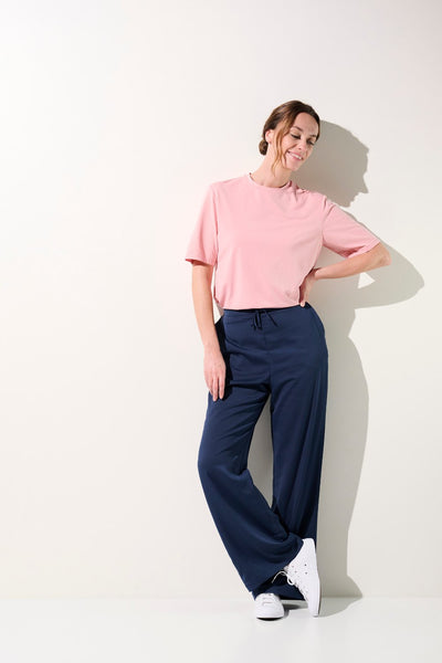 Femme en t-shirt anti-UV rose, confortable et élégant, associé à un pantalon ample pour un look décontracté.
