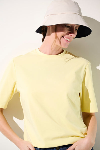 Femme portant un bob anti-UV - Faro beige et t-shirt jaune léger, parfaits pour la protection solaire quotidienne.