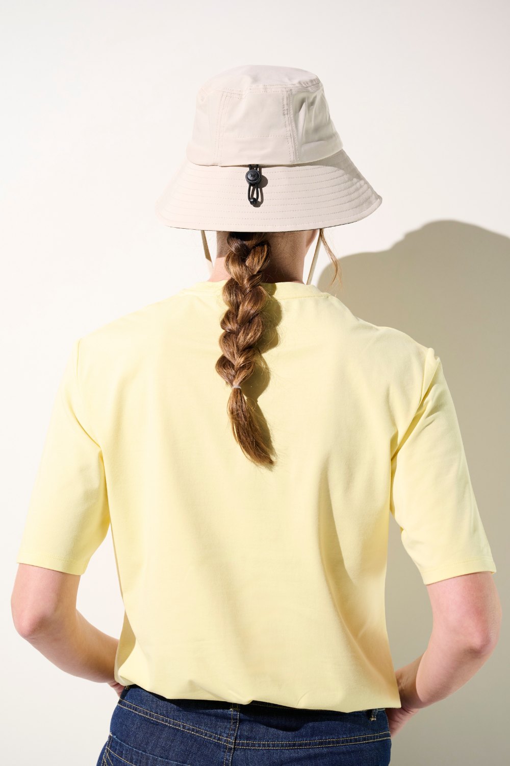 Femme portant un bob anti-UV - Faro beige avec un t-shirt jaune, offrant une protection solaire efficace.