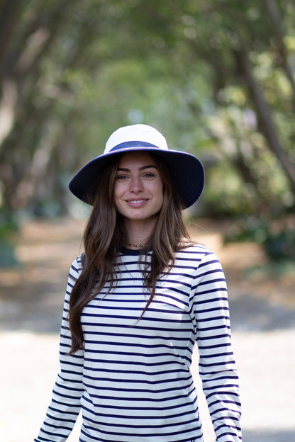 Femme souriante portant un t-shirt anti-UV rayé et un chapeau ensoleillé, idéale pour la protection solaire UPF 50+.